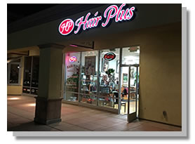 Night view of the pink Hair Plus sign and circular HP logo over the glass storefront